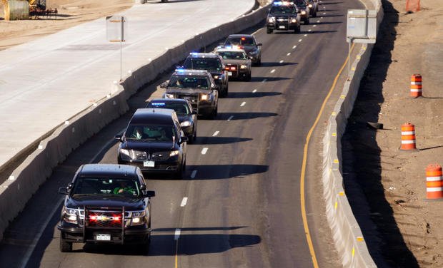 A procession of police vehicles escorts the hearse carrying the body of a deputy killed in a domestic disturbance where multiple deputies and civilians were shot in Highlands Ranch 